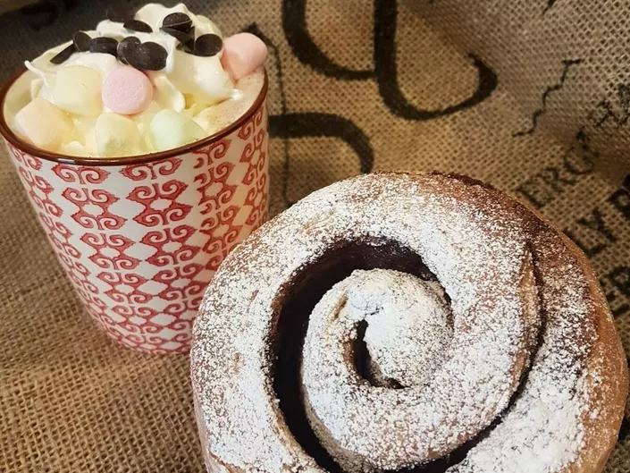 Nærbilde av en kanelsnurr og kakao med krem