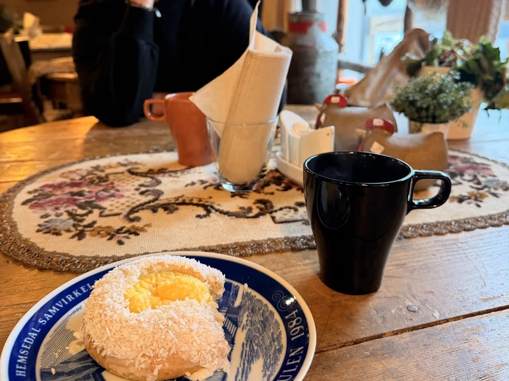 En jente som er på kafe på Hemsedal Flatbrødbakeri med kaffekopp og skolebrød på tallerken