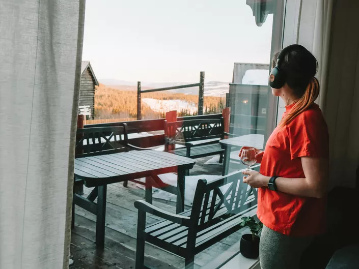 Kvine står til høyre for bilde og ser ut av vinduet med svarte hodetelefoner