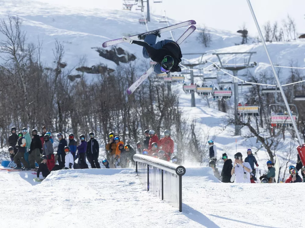 Gutt som gjør et triks i en rail i parken, og i bakgrunnen står publikum og heier.