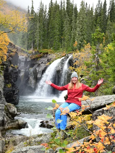 Høstbilde av Rjukandefossen med kvinne som holder to hende opp til siden i front