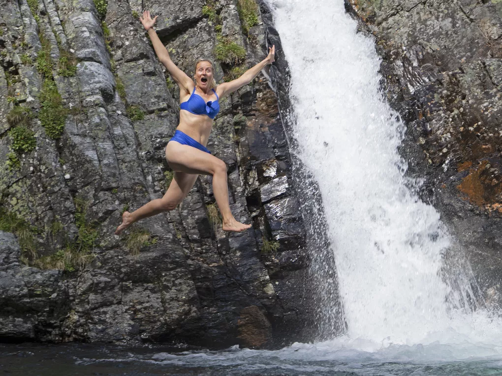 Dame som hopper med armene ut, fossefall.