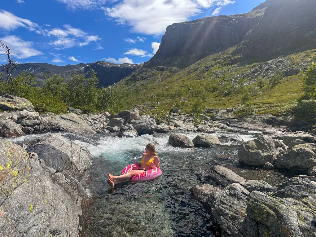 Dame som sitter i donut i elva (sommer) og ser utover fjellene i Hemsedal.