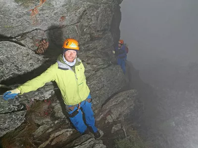 To menn som klatrer i fjellvegg, i dis og tåke.