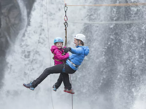 Mor og datter som kjører zip line ved en foss i Hemsedal