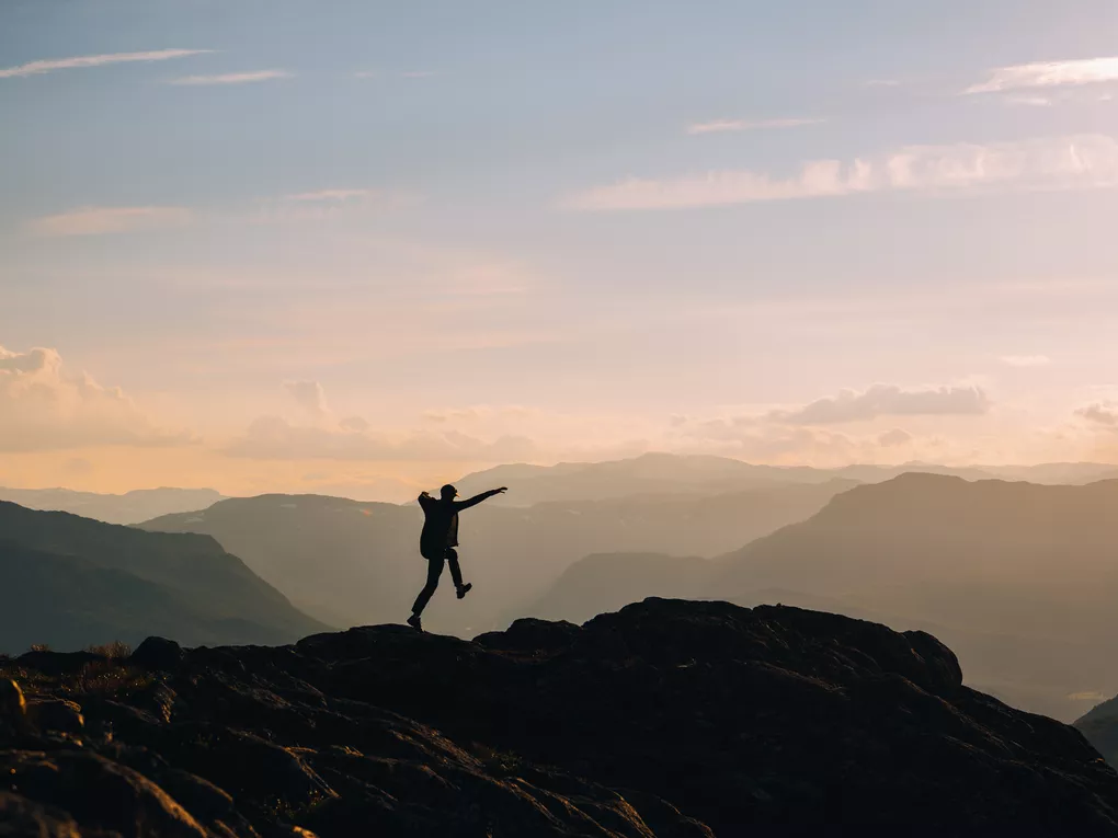 Person på et fjell i morgen disen, hopper i lufta.