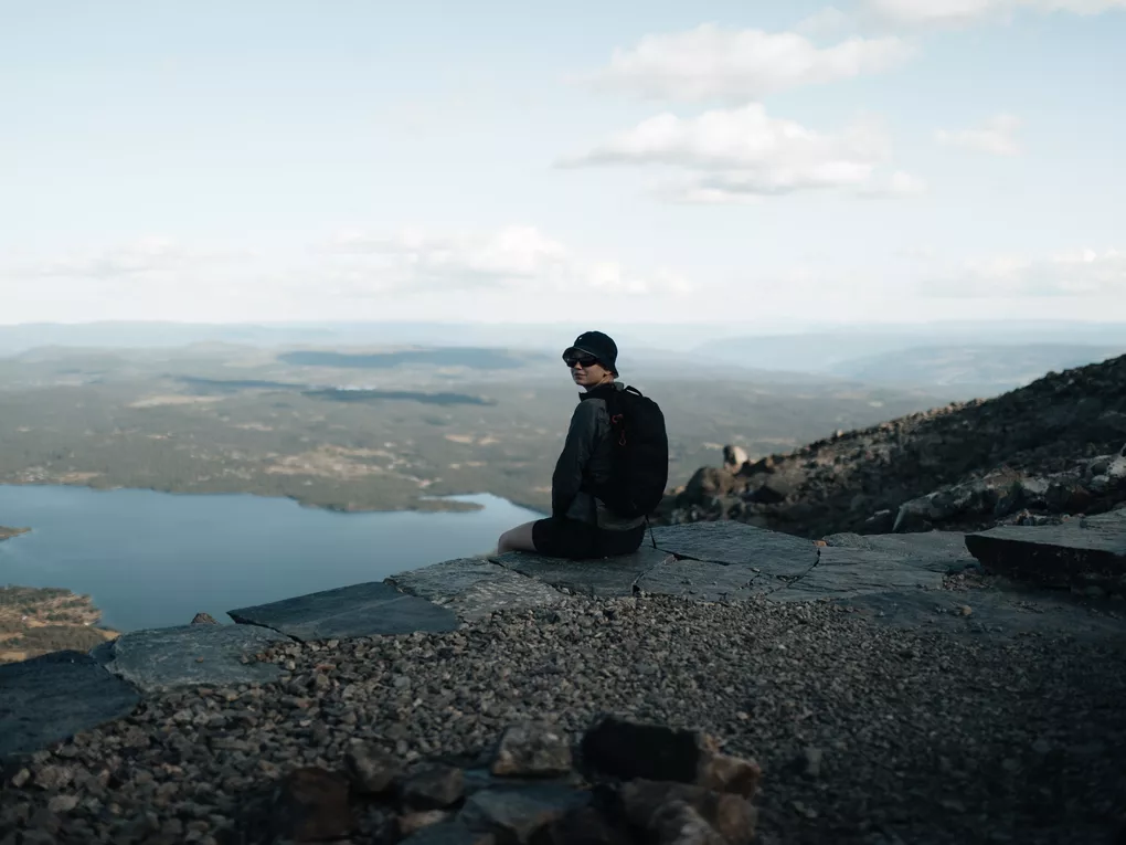En dame ikledd bøttehatt, som sitter på en av trappetrinnene på veien opp/ned Skogshorn.