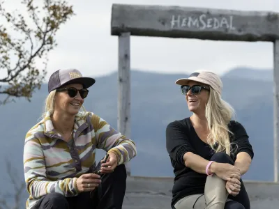 To damer som sitter ved Hemsedal skilt på toppen av storhøvda