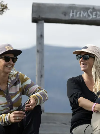 To damer som sitter ved Hemsedal skilt på toppen av storhøvda