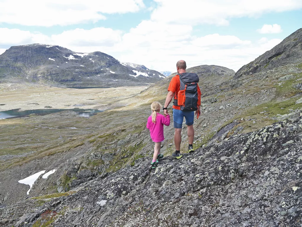 Mann og liten jente, holder hender i fjellet.