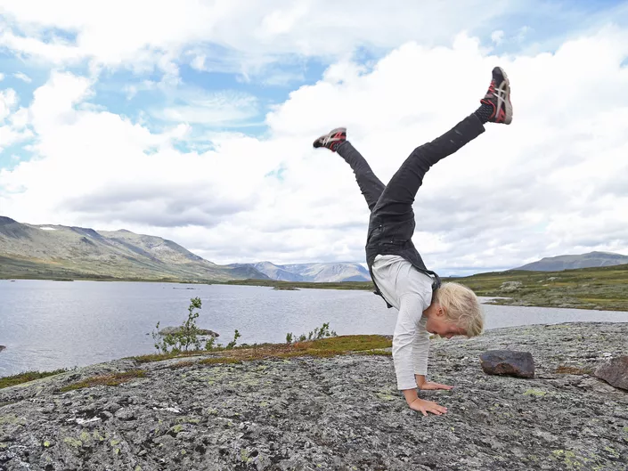 Liten gutt som står på henda i fjellet.