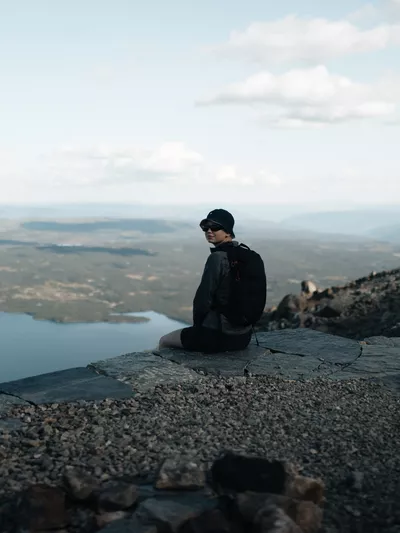 En dame ikledd bøttehatt, som sitter på en av trappetrinnene på veien opp/ned Skogshorn.