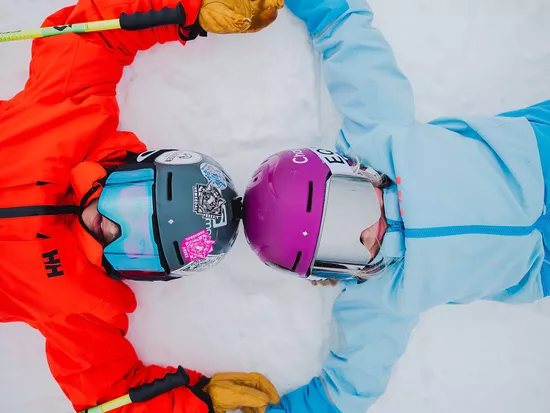 Jente og gutt som ligger på snø i skiklær og har hendene over hode og ser inn i kamera i Hemsedal