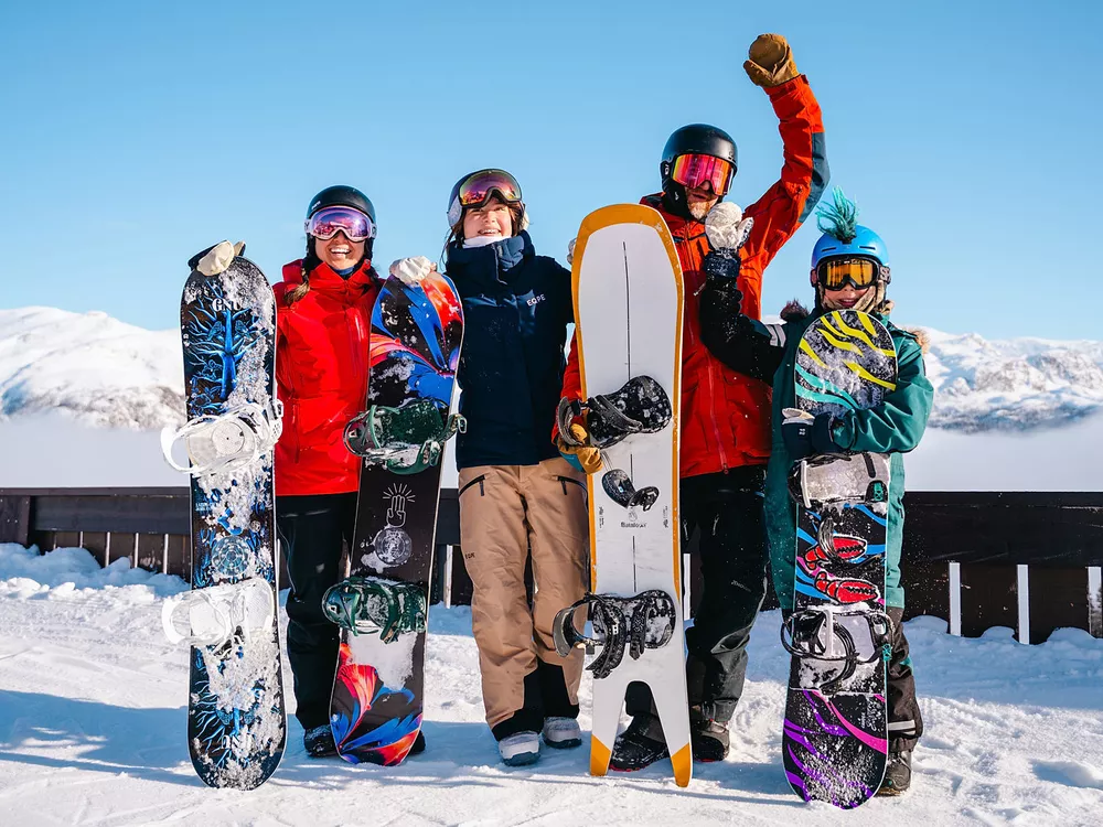 Familie som kjørt snowboard i Hemsedal. De er glade og har hendene i luften